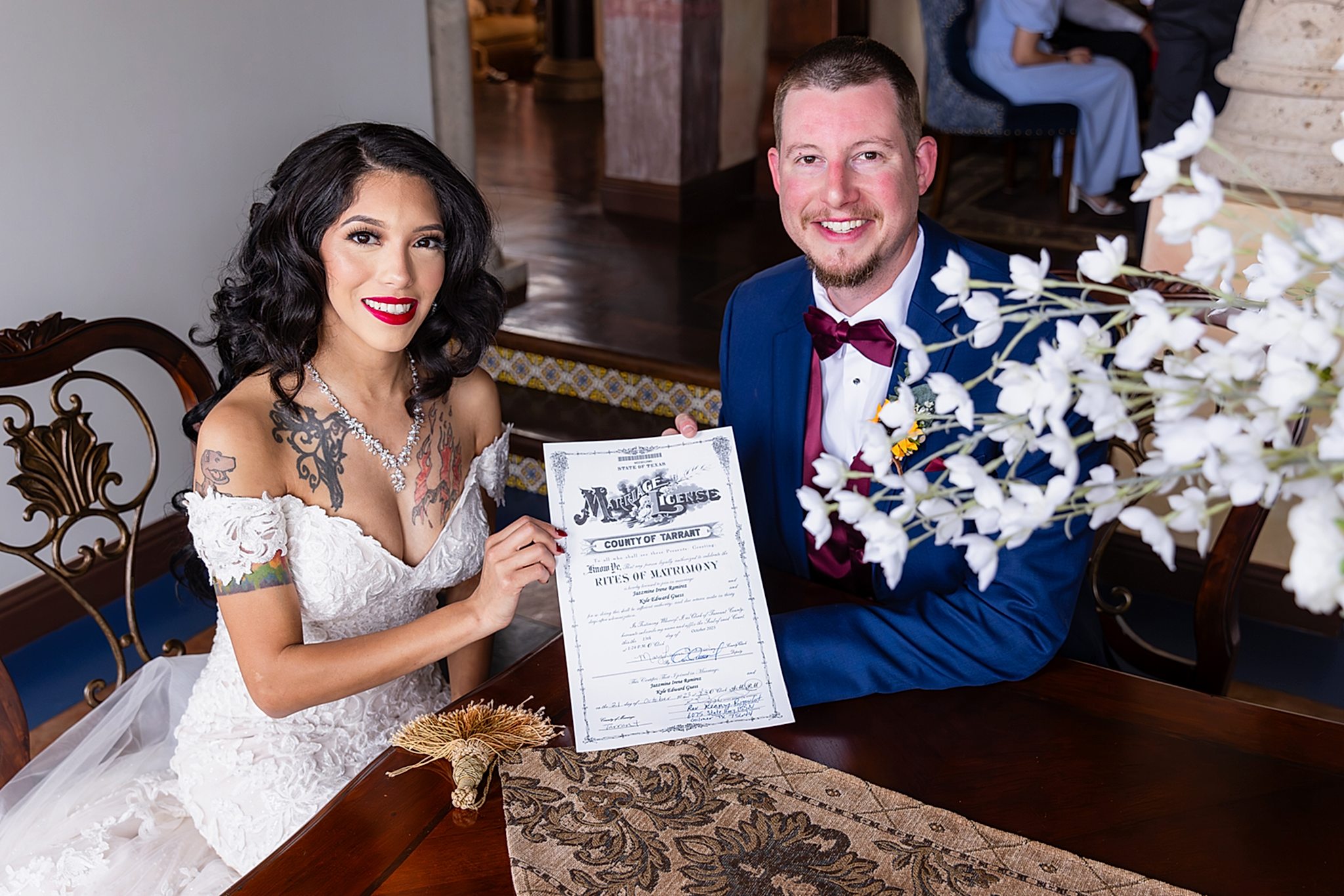 Tattooed bride and groom in navy suit smiling while holding signed marriage license at table in Stoney Ridge Villa wedding venue